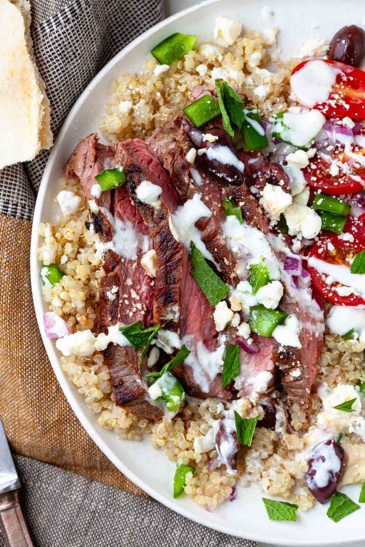 steak grain bowl drizzled with herb yogurt sauce and garnished with fresh chopped mint.