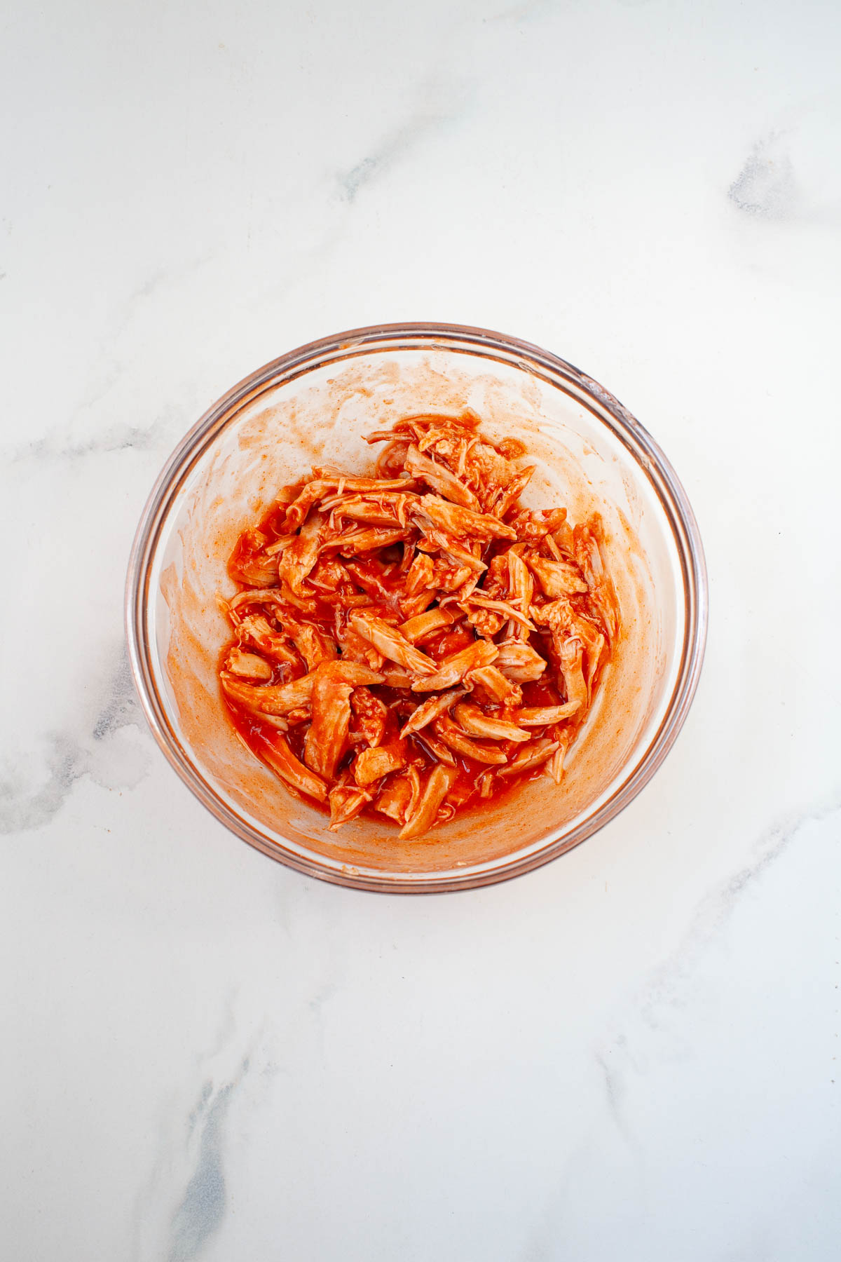 shredded chicken in buffalo sauce in glass bowl on marble surface