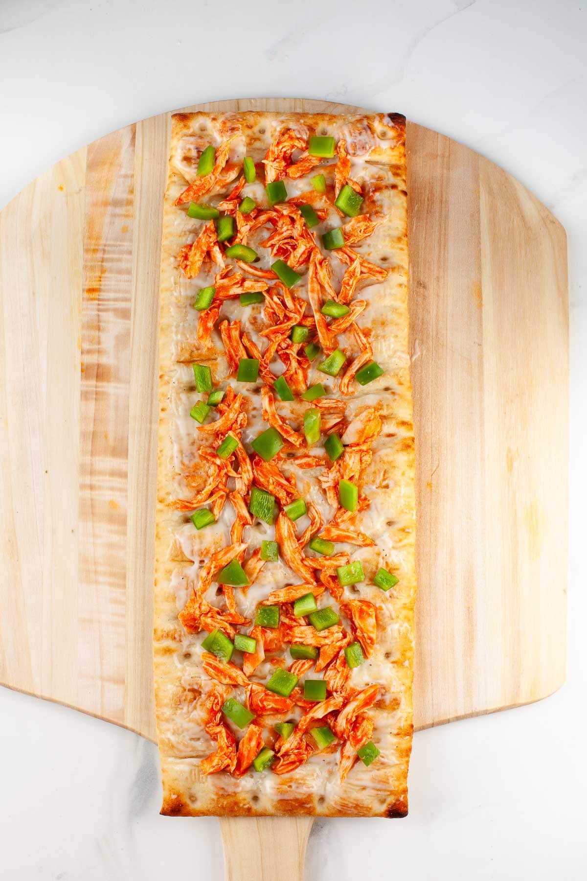 flatbread with buffalo chicken and green bell pepper on wood pizza peel