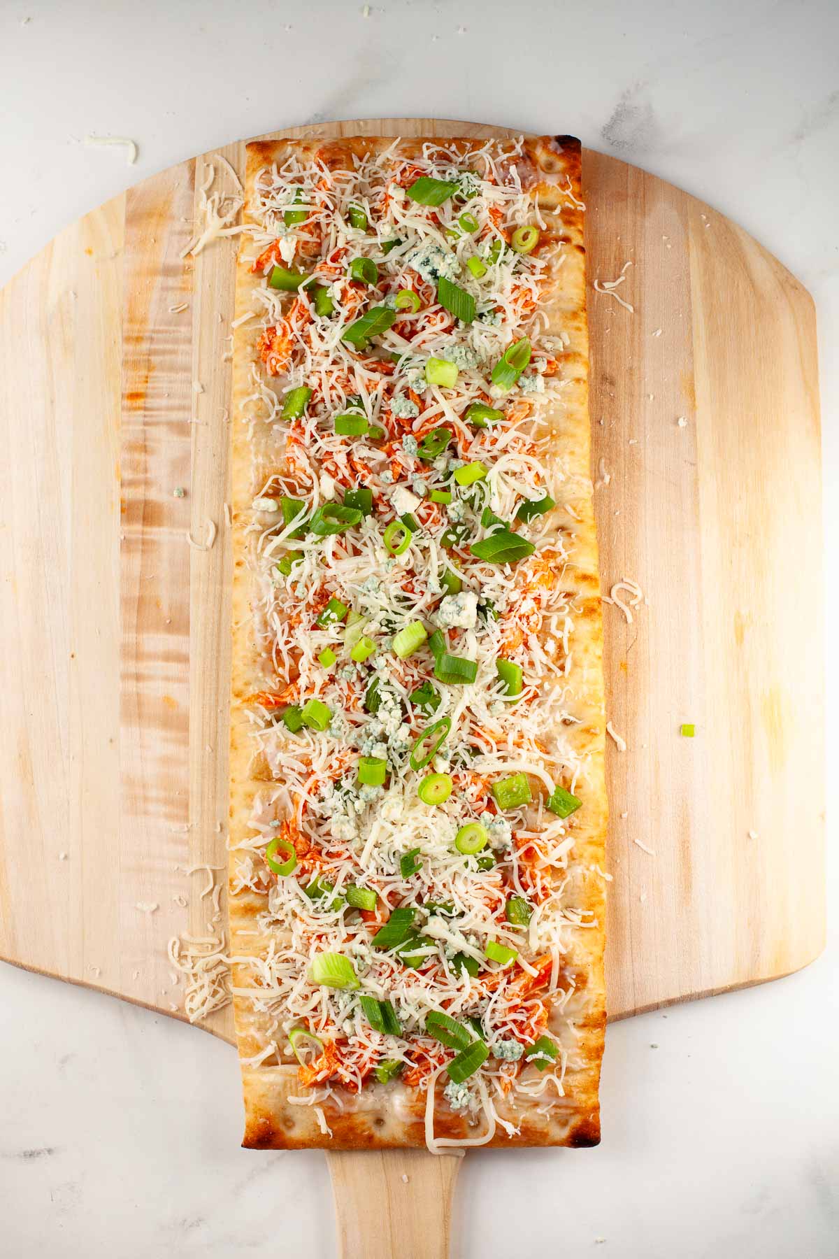 flatbread with buffalo chicken, bell pepper, cheese and green onion on wood pizza peel