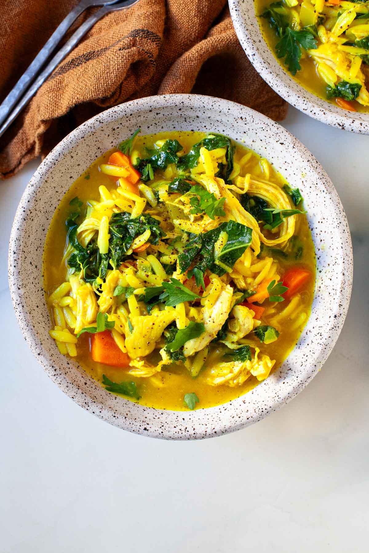 speckled bowl with chicken orzo soup with turmeric, kale, carrots and parsley next to another soup bowl