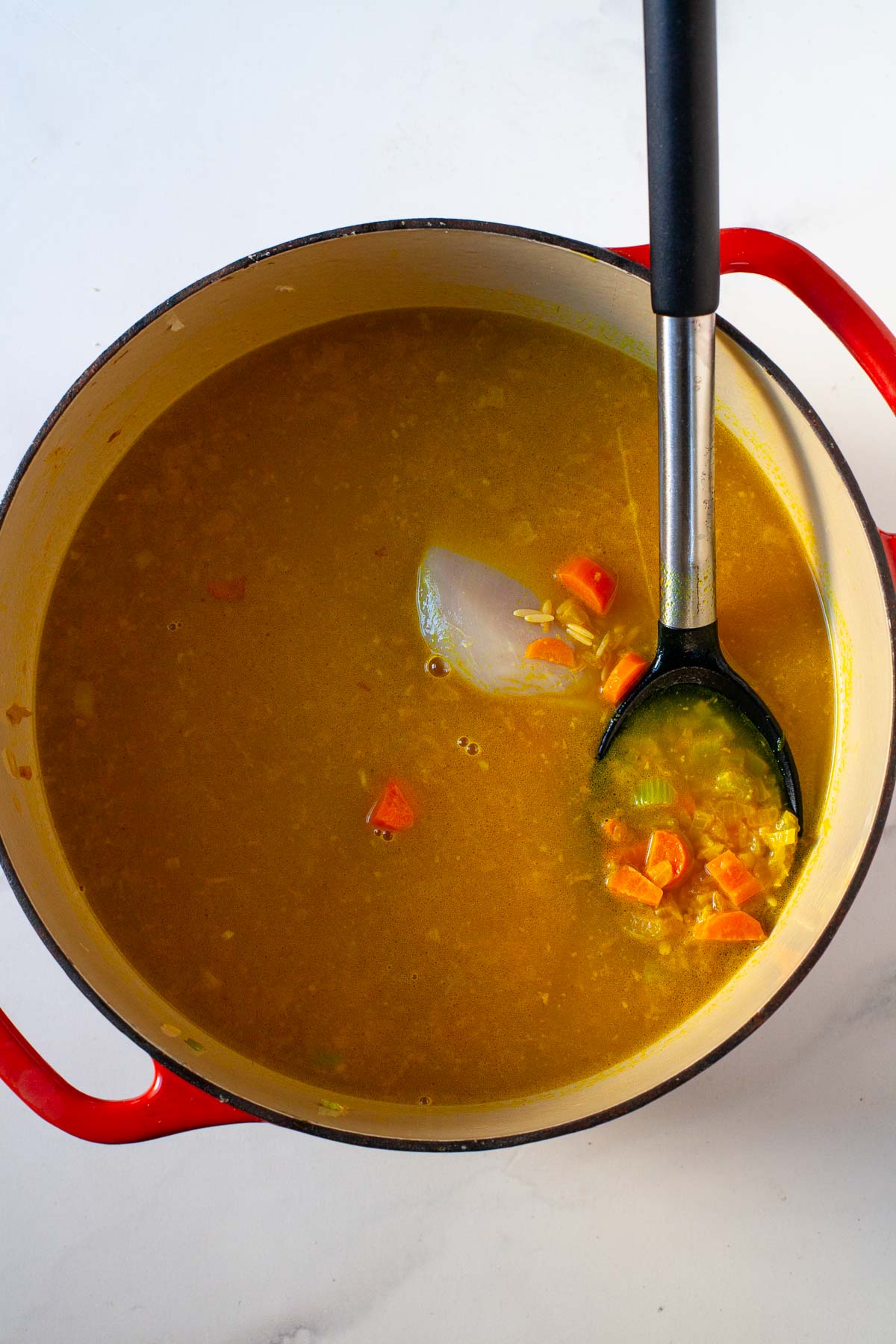 chicken soup before boiling with broth and raw chicken in red dutch oven with black mixing spoon
